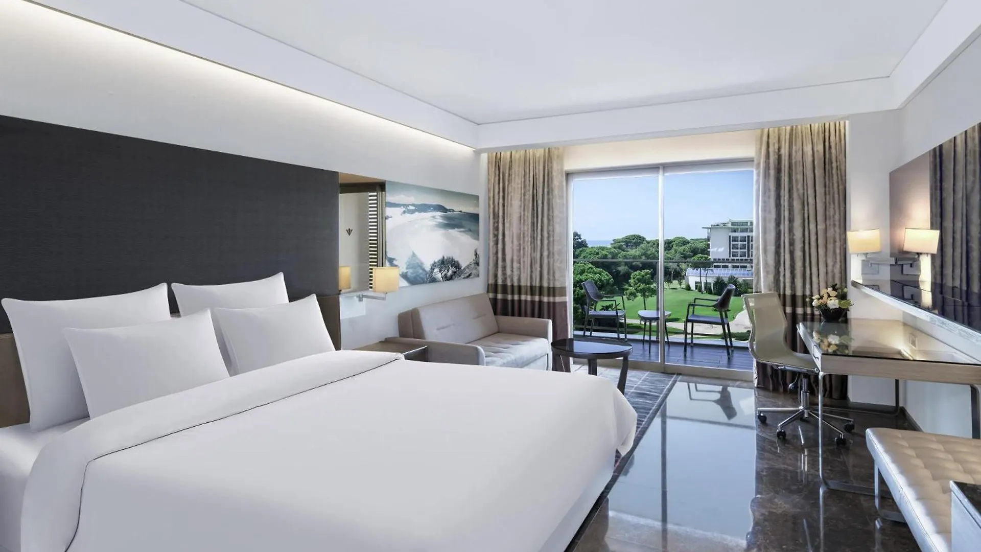 Rixos Premium Belek - The Land Of Legends Access Hotel Exterior photo The photo shows a bright and spacious hotel room with a contemporary design. The focal point is a large, comfortable bed with crisp white linens and several pillows, positioned centrally in the room. 

Behind the bed is a dark gray upholstered headbo
