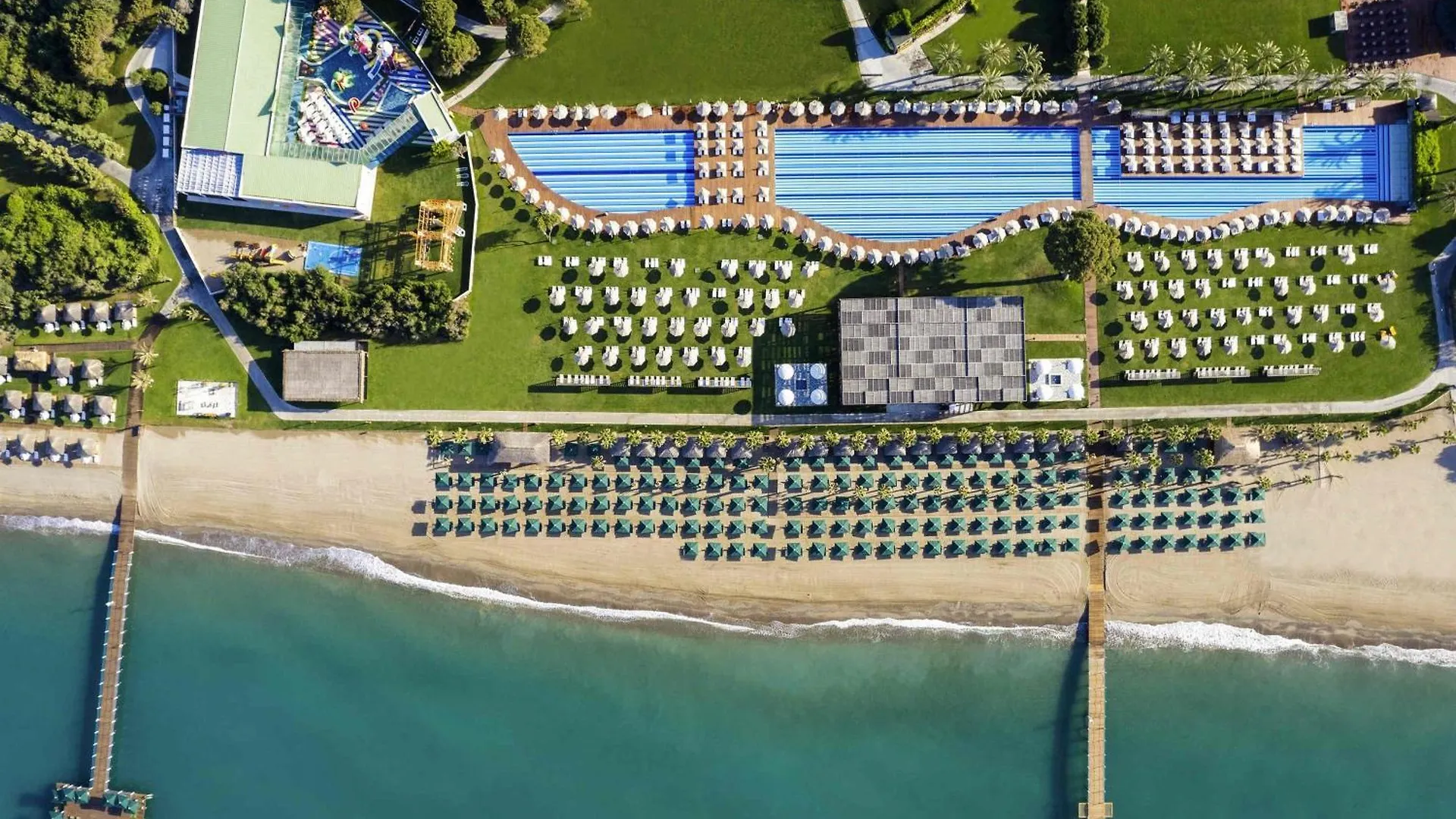 Rixos Premium Belek - The Land Of Legends Access Hotel Exterior photo This is a high-angle, aerial view of a large, luxurious resort complex situated between lush green grounds and a sandy beach leading into the sea.

**Key features in the image include:**

*   **Swimming Pool Area:** The centerpiece of the resort is a